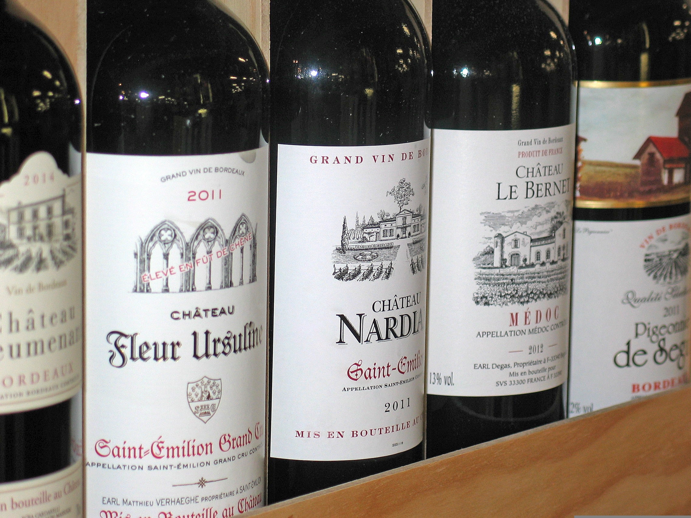 Bouteilles de bordeaux alignées dans une caisse en bois, étiquettes de Saint-Émilion et de Médoc