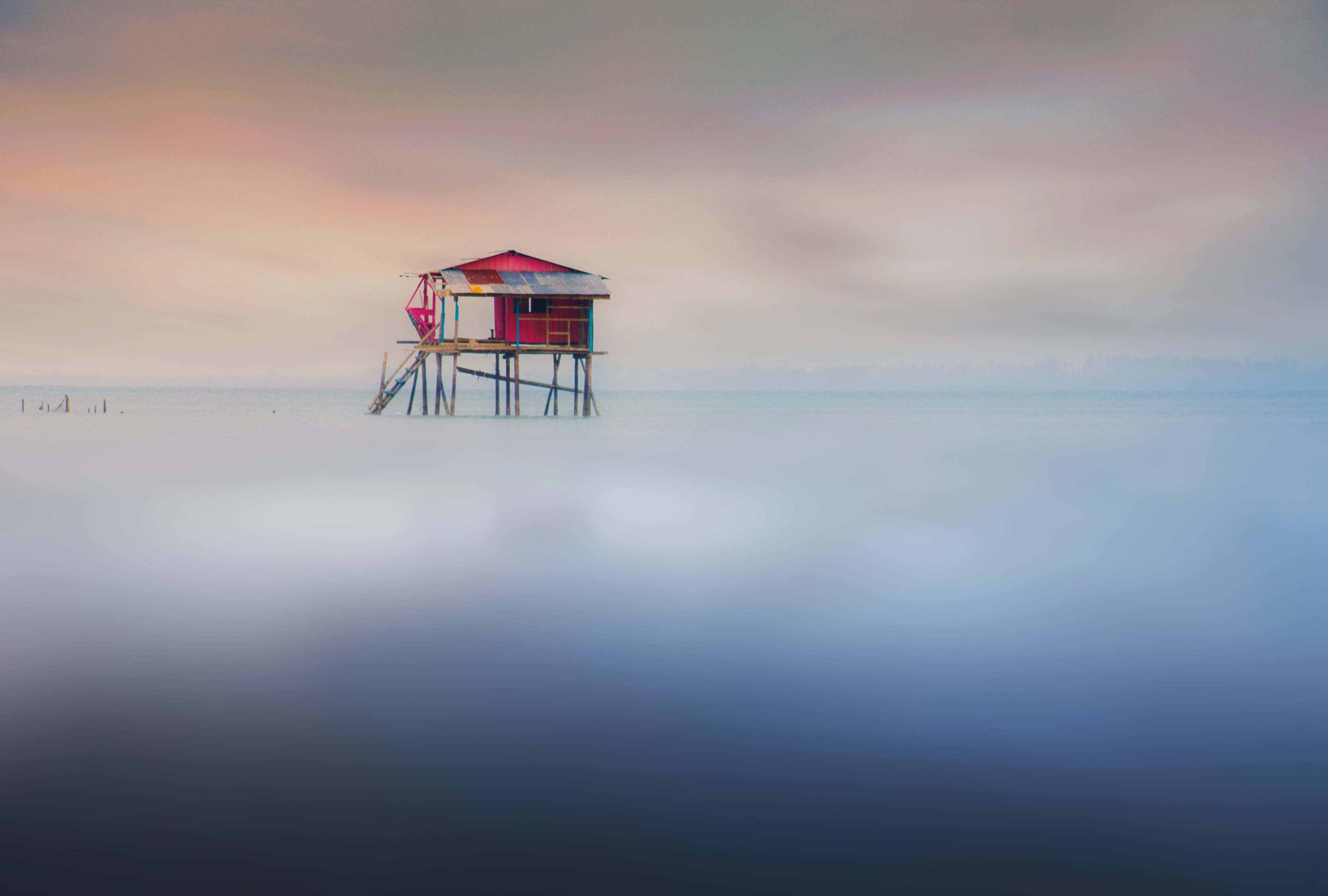 Maison sur pilotis au-dessus d’une eau calme, ciel pastel à l’aube